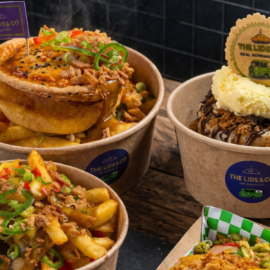 Assorted takeaway dishes from The Lids & Co, including a golden-brown pie served on thick-cut chips with gravy and toppings, a loaded fries bowl garnished with spring onions and chilli, and a dessert pie topped with vanilla ice cream and chocolate sauce, all in branded cardboard bowls on a rustic wooden table.