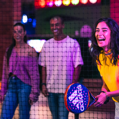 A woman wearing a yellow top and smiling while playing a ball game while holding a paddle.