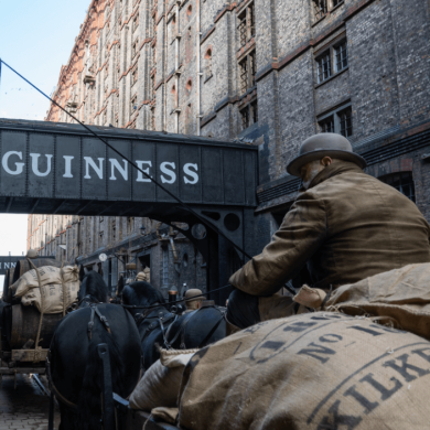 A large brick building with a sign that says Guinness on it and horse and carts pulling large sacks.