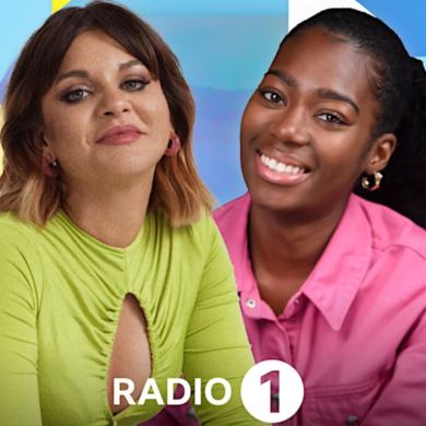 Two people who are radio DJS for the BBC. One is wearing a green top and one is wearing a pink top.