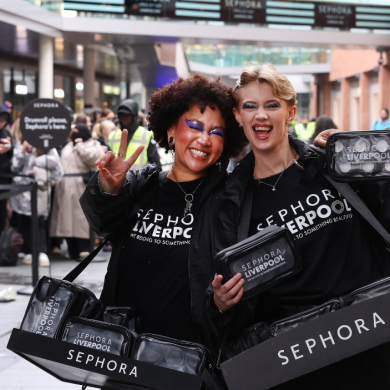 Two people wearing makeup stood smiling and holding Sephora bags.
