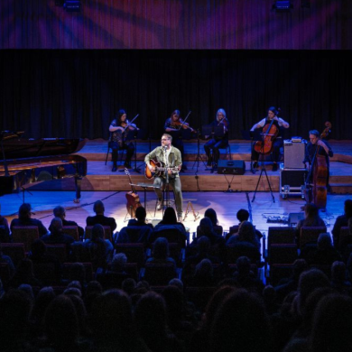 A band performing music while standing on stage with a crowd watching them.