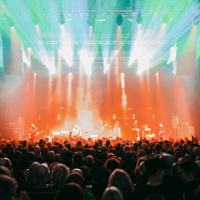Inside of a music venue in Liverpool with a large crowd and orange and green lighting.