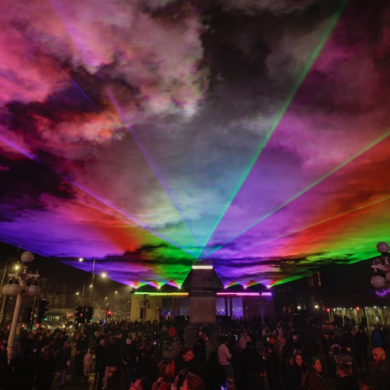 Lightport at Monument Square in Southport, image shows rainbow coloured lasers over a crowded Monument Square