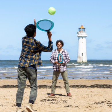 A father and son play tennis on New Brighton beach with New Brighton lighthouse in the background.