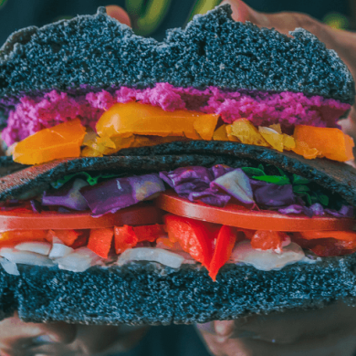 A black burger bun packed full of peppers, cabbage and tomatoes