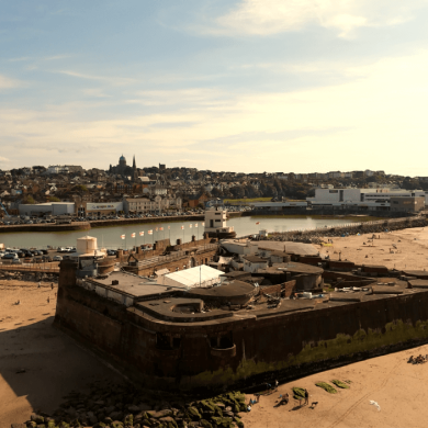 An old fort on a beach with a town behind taken on a drone