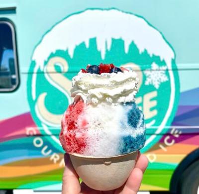 Person holds up snow cone with red, which and blue flavoring and toppings