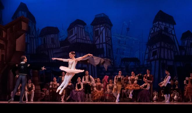 Ballerina dancing in spotlight on stage with other dancers in the background