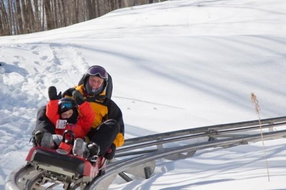 A man and child ride a coaster on rails through the snow