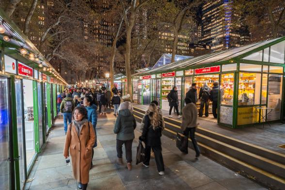 Bryant Park Holiday Market Holiday market at night in Bryant Park with people browsing stalls under lit trees.