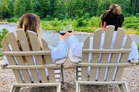 Emerson Resort Two women in robes clinking wine glasses, sitting in Adirondack chairs overlooking nature