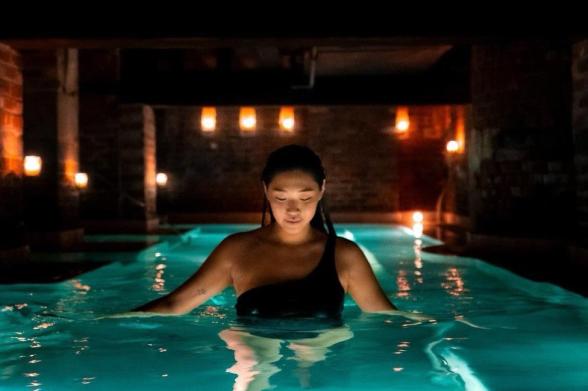 AIRE Ancient Baths NYC A woman walks through a pool in a candle lit room at AIRE Ancient Baths NYC