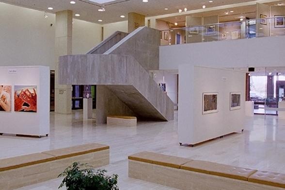 Dyer Arts Center Art hangs on the white walls surrounding a grey central staircase in the gallery of the Dyer Arts Center