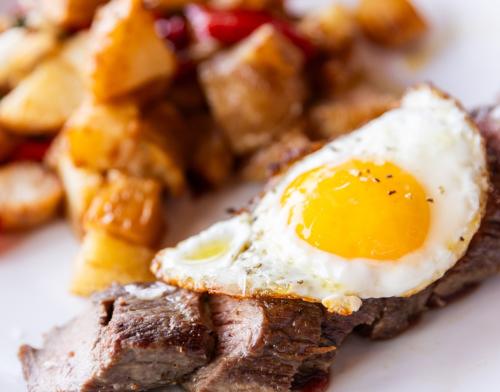 Steak strips with a fried egg on top and breakfast potatoes