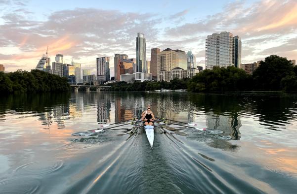 Rowers moving towards the downtown skyline on glassy, reflective water.