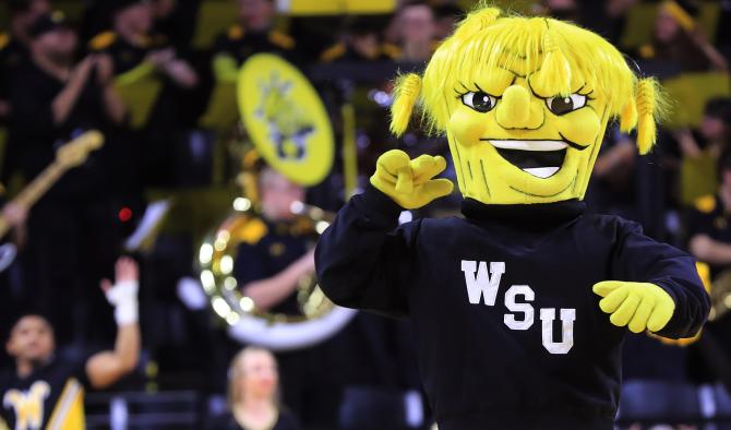 The Wichita State Shockers mascot WuShock walks in front of the school's marching band during a college basketball game.