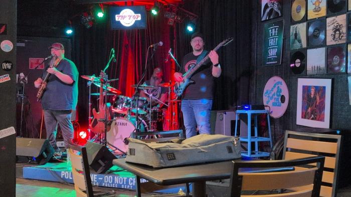 Live band performing on stage at Tip Top Cafe, surrounded by colorful stage lighting and music memorabilia.