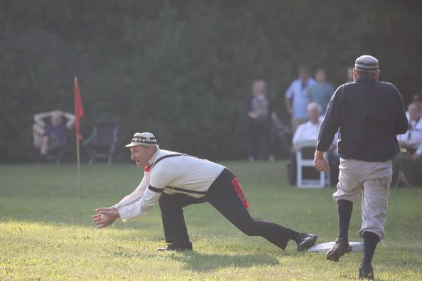 A vintage base ball player reaches with bare hands to catch the ball during a game on the fort ball grounds at Mackinac Island's historic Fort Mackinac