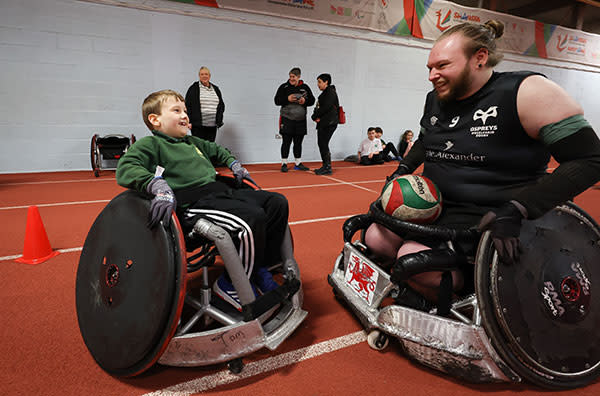 A boy in a wheelchair smiling at a wheelchair rugby player.