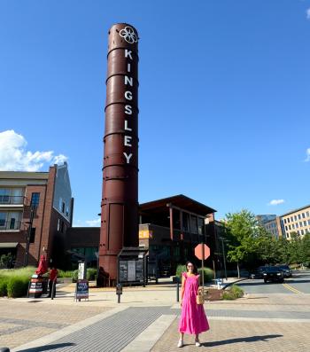A woman in a pink dress strolling along Kingsley street in Fort Mill, SC, with a smoke stack visible.