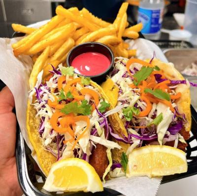 Person hold up plate of two fish tacos and a side of fries