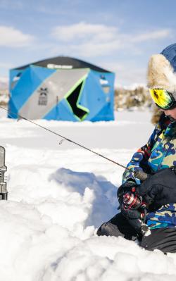 A child sits in the snow on frozen Grand Lake ice fishing.