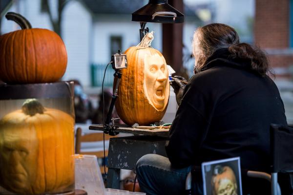 Man carving intricate face onto pumpkin