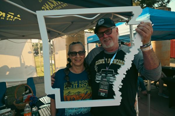 A couple hugs while holding out a white cutout of the state of Arkansas.