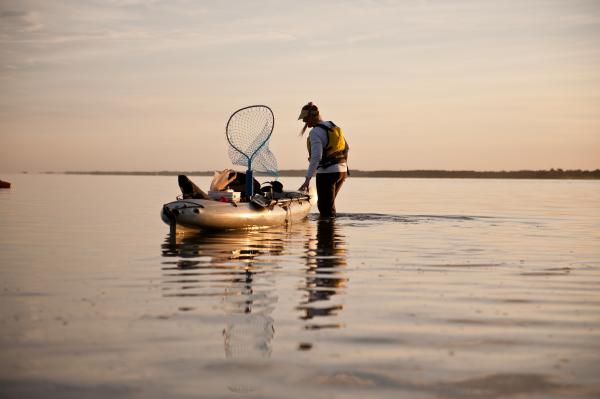 guy walking in shallow water with fishing kayak