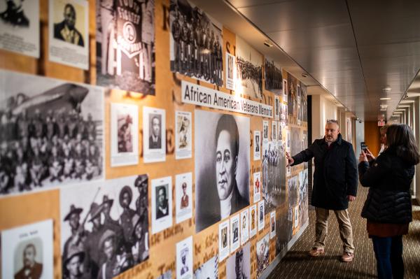 a tour guide showing a group a wall of photos representing African American veterans of war