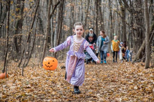 Little girl in princess dress running along a trick-or-treat path in the woods