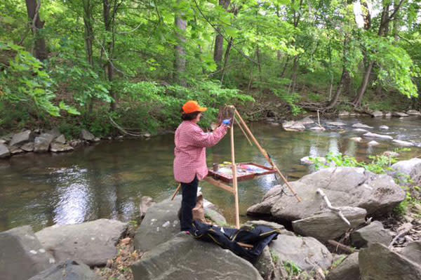 a women painting by creek standing on Boulders