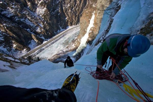 an ice climber looking down at other climbers on a frozen waterfall