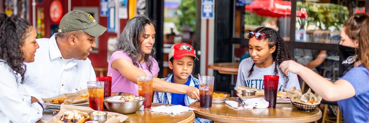 Family and friends gathered around an outdoor restaurant table sharing food and drinks together