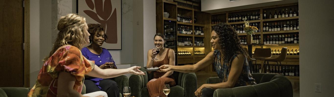 A group of women sit in a cozy wine cellar while enjoying chocolate treats.