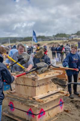 A team of sandcastle contest participants scoops sand with a shovel and puts it into a pile.