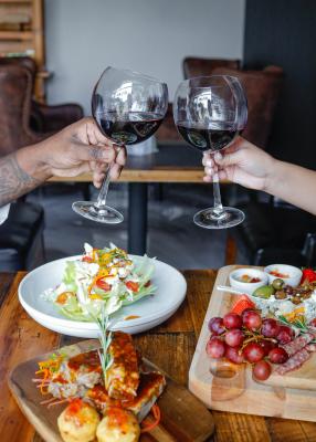 Two hands with wine glasses cheersing over a table filled with charcuterie boards