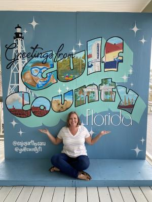 a young lady sitting cross legged infront of a post card type mural