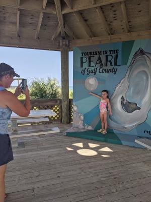 an older lady taking a photo of a little girl on a mural with an oyster and pearl background