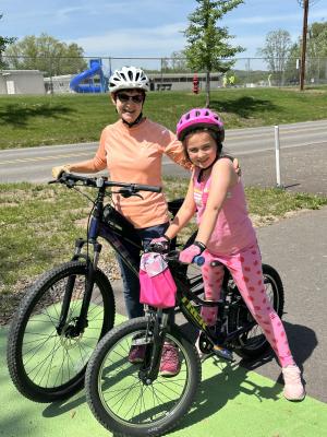 Two girls perched on bikes and smiling in the sunshine of a pretty summer day.