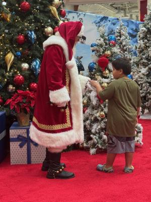 Young boy with autism gently holding Santa’s hand, captivated by the sparkling Christmas tree decorations