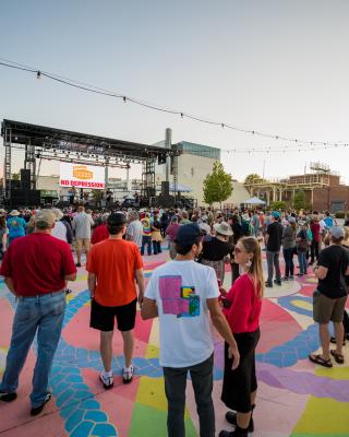 People in a crowd stand in front of a stage with a music performance going on.