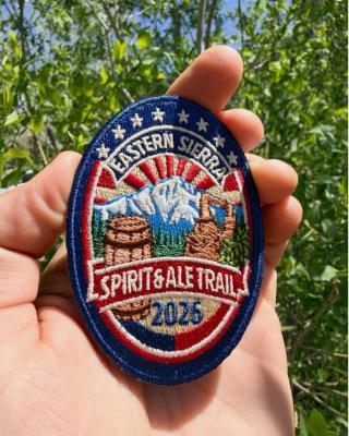 The 2026 patch for the ale and spirit trail - oval, with those words and year - with mountains, and barrel, and red, white and blue stars and stripes similar to the US flag.