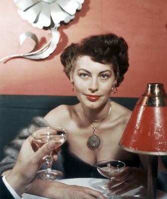 Ava Gardner drinking champagne with someone across the table who is mostly out of frame