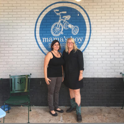 Mama's Boy owners Alicia Segar and Cooper Hudson stand in front of the Mama's Boy logo.