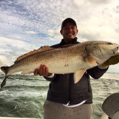 A smiling fisherman holding a large redfish caught near Daytona Beach