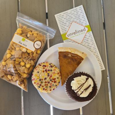 Cookie, pie slice, and chocolate cupcake on a plate next to a bag of chex-mix.