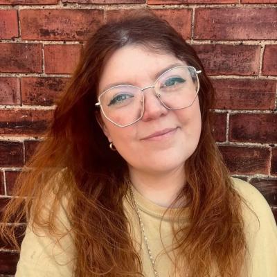A photo of Hull artist, Lauren Saunders smiling in front of a brick wall in a yellow top.