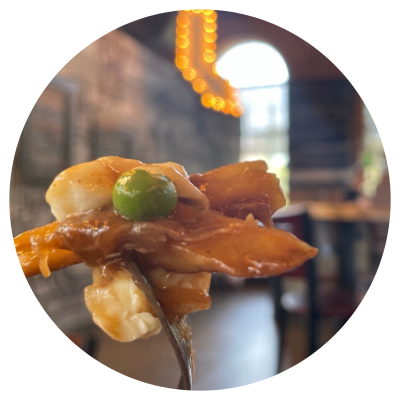 A fork with the perfect bit of a braised beef poutine with cheese curds and a pea